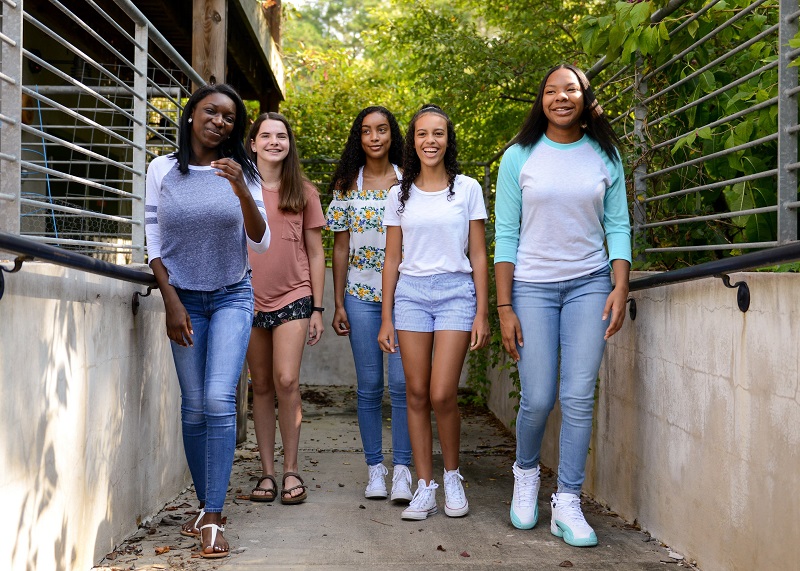 five middle-school and high-school aged girls walking down sidewalk by school building