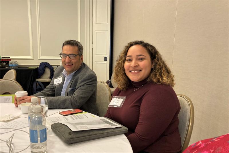 Alan Cabo-Lewis and Chabely Figuereo sit at round table in large conference room