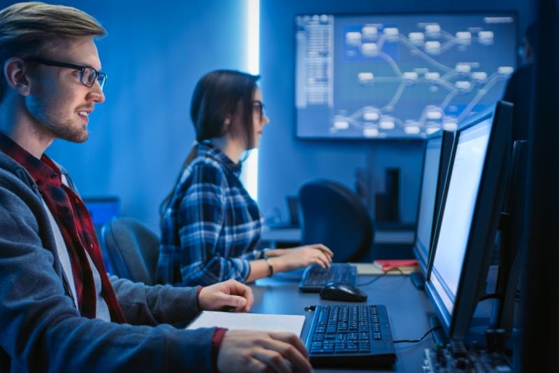 two IT workers at laptops in communal office space with blue background