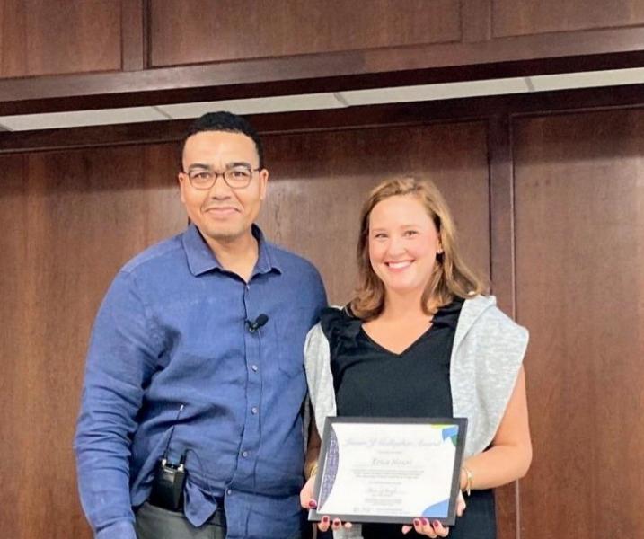 Brian Boyd at left, Erica Nouri at right, both smiling at camera with wood panel background