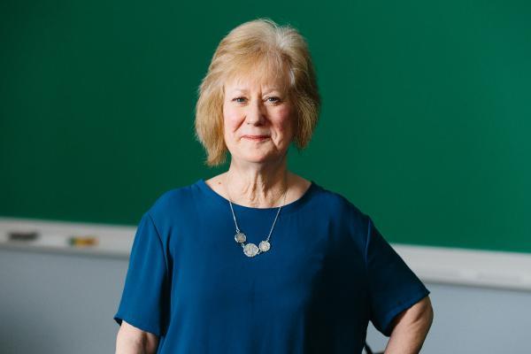 Harriet Able is a white woman with short blonde hair. She is wearing a blue top and necklace.