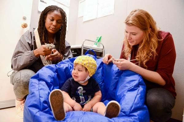 two female researchers in lab setting monitor cap on toddler boy
