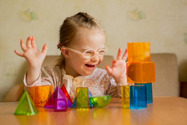 A girl with Down's syndrome wearing glasses lays out geometric shapes on a table.