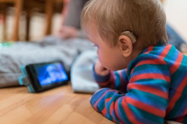 baby with hearing aid is watching animated tale on smartphone