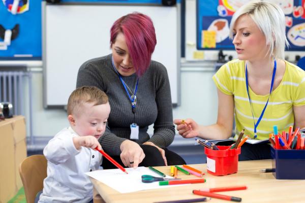 two teachers working in classroom at small round table with young boy with down syndrome