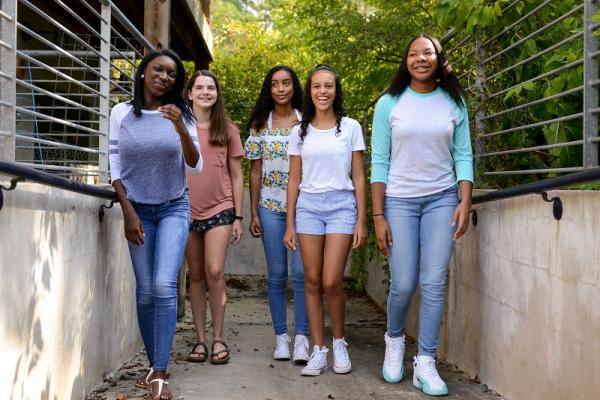 five middle-school and high-school aged girls walking down sidewalk by school building