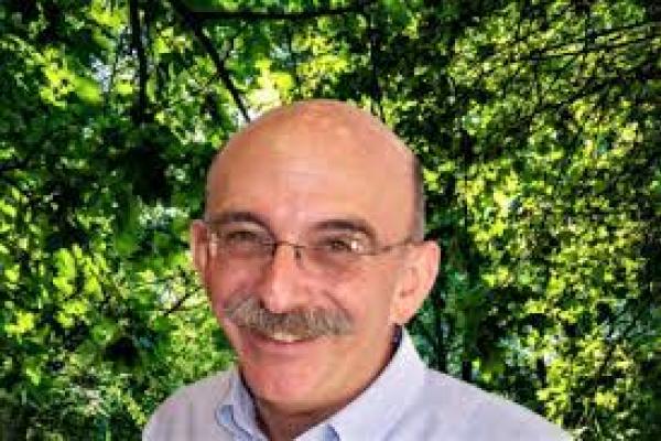 peter ornstein; bald man with glasses and mustache stands in front of tree smiling at camera