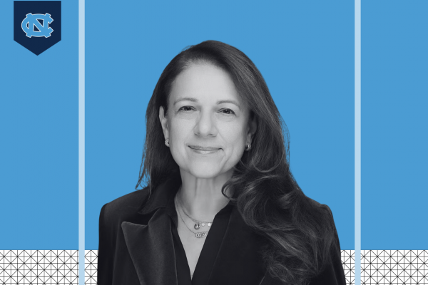 Ayse Belger; black and white headshot style photo of woman smiling with interlocking NC UNC logo at left and carolina blue background