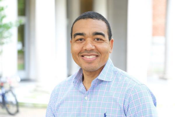 Brian Boyd; man wearing light blue button up shirt stands outside on UNC's campus, smiling at camera