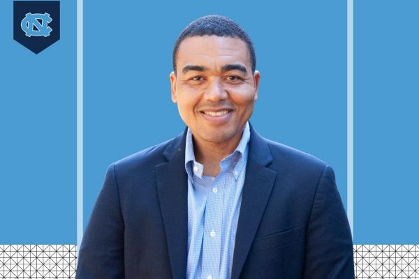 Headshot style photo of Brian Boyd smiling at camera with interlocking NC UNC logo in top left corner and carolina blue background