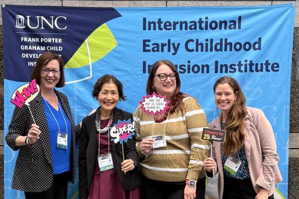four attendees at the international early childhood inclusion institute standing in front of decorative event sign