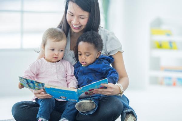 woman holds two toddlers in her lap while reading a book to them