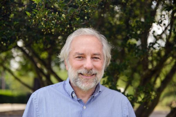 headshot of ronald seifer; man with gray hair wearing blue oxford shirt standing outside in front of green tree