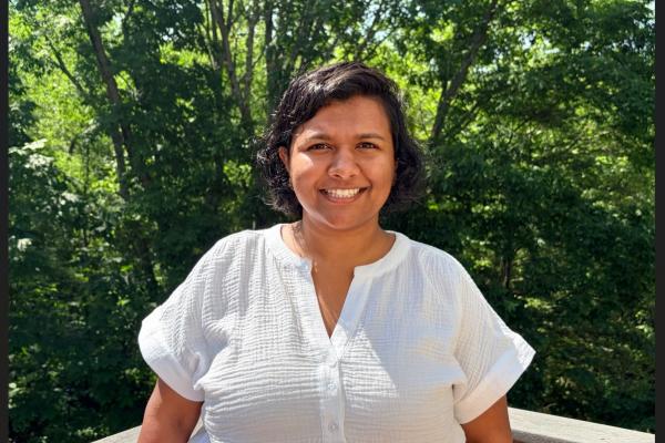 Aditi Nambiar; headshot style photo of woman with short dark hair and wearing a white top smiles at the camera