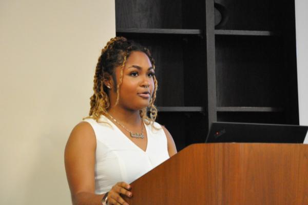 Aerryan Bentley; young woman in white top stands behind lecturn giving a presentation