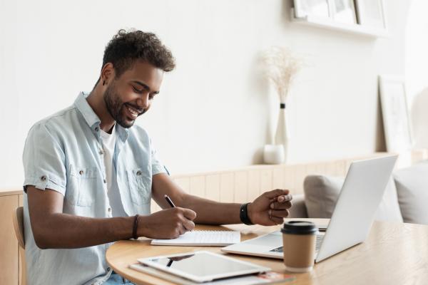 A man takes notes while looking at his computer.