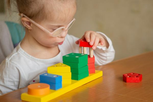ittle girl with Down syndrome learns to assemble an intricate pyramid using multicolored geometric shapes