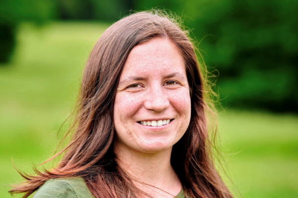 headshot of brianne tomaszewski smiling at camera while standing outside with greenery behind her