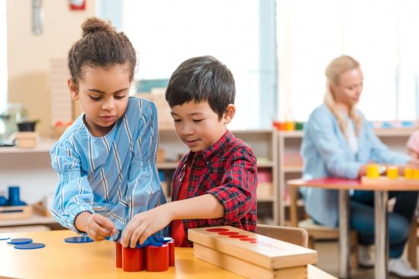 young girl and boy using building shapes at small table in classroom