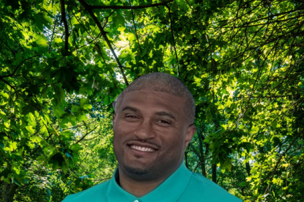 correy watkins; man wearing teal shirt stands in front of trees and smiles at camera