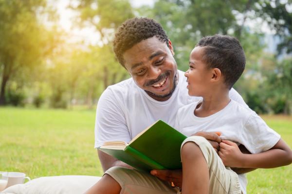Smiling African American son and father having a picnic in the park while reading a book together