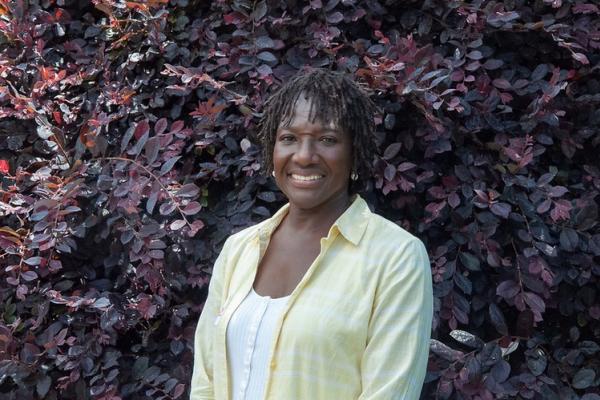 Denise Bennett stands in front of dark purple shrubbery