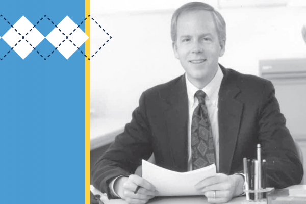 Black and white photo of Don Bailey sitting at a desk with Carolina Blue accent at left and argyle pattern