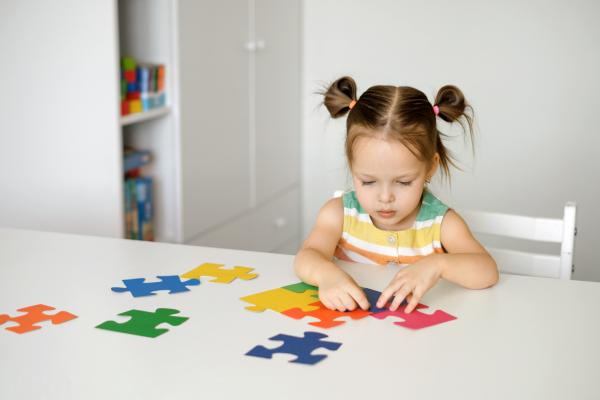 young girl puts pieces of a colorful puzzle together atop a white table
