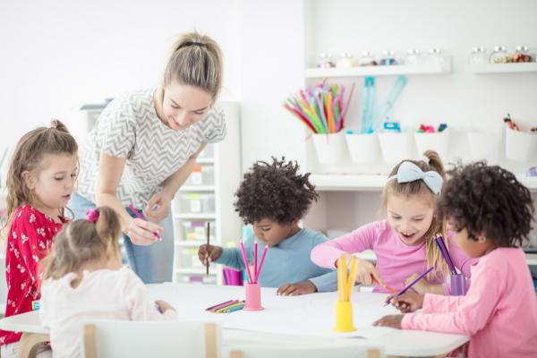 a group of young children work at a table with teacher standing by