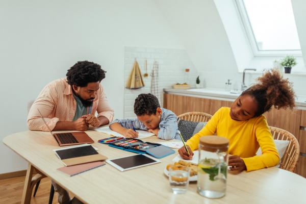 Two children being home-schooled by their father while sitting at the kitchen table