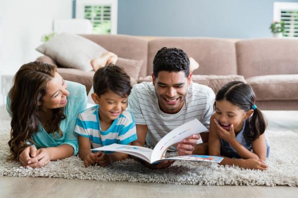Parents and children lying on rug and reading book in living room at home