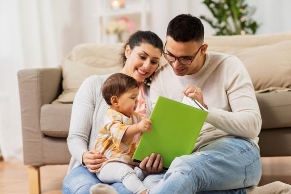 family, parenthood and people concept - happy mother, father and baby daugter reading book at home