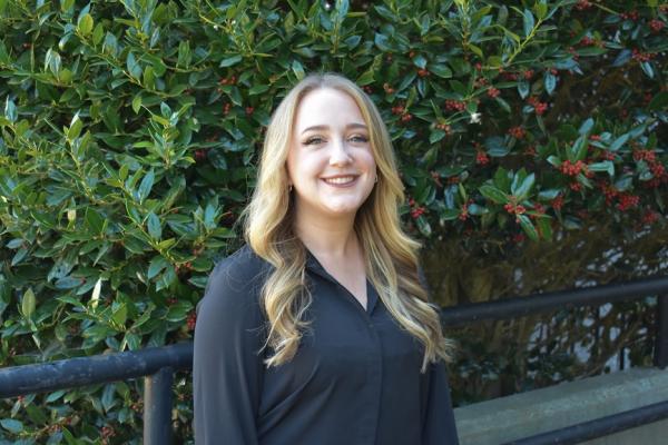 lindsay gomes; woman with long blond hair stands outside in front of shrubbery and smiles at camera