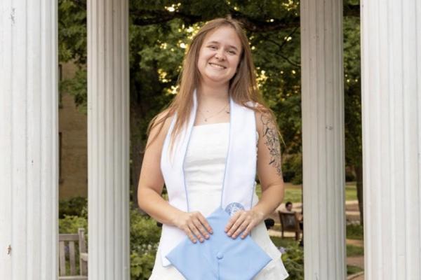 Haylie Bledsaw; young woman stands outside in with carolina blue graduation cap in her hands