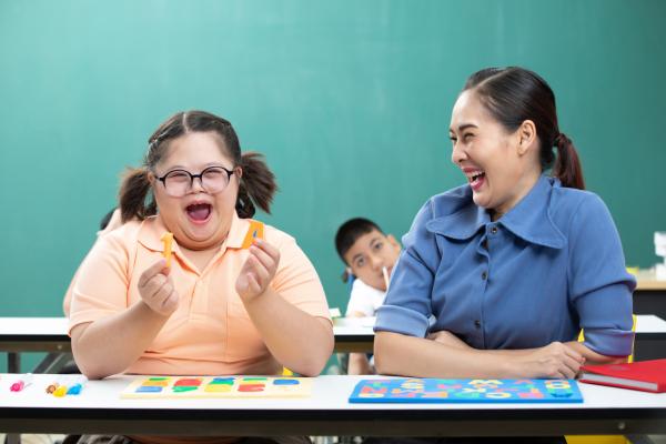 A disabled student holds alphabet toys while working with a teacher