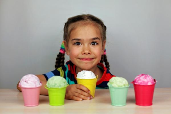 young girl with dark braids sits at table with five servings of ice cream in front of her inside colorful cannisters