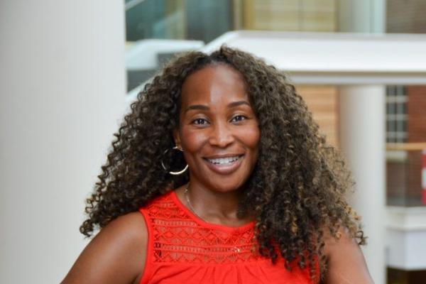 Iheoma Iruka; Black woman with shoulder-length hair and wearing red top smiles at camera