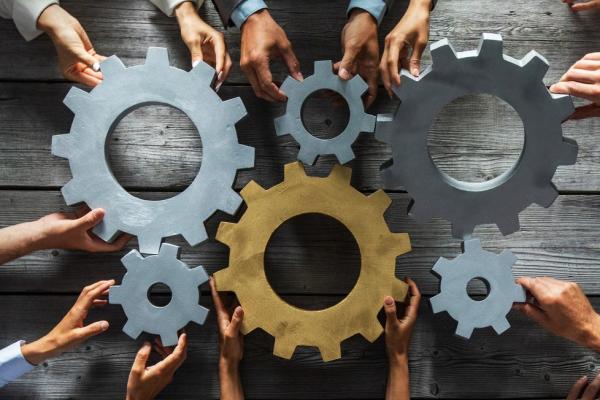 Group of business people joining together silver and golden colored gears on table at workplace top view