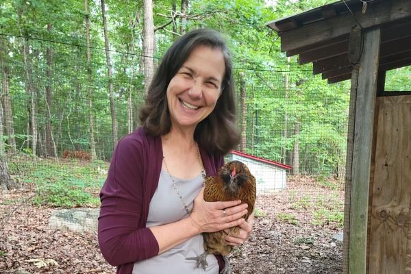 Jennifer Stone; woman stands outside holding a red hen