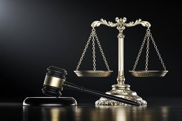 silver justice scales on table with black background and mallet gavel in foreground