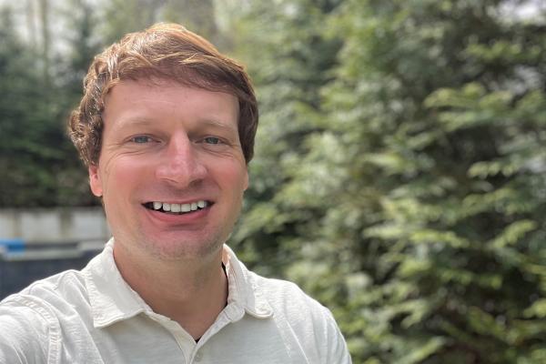 Kellen Reid; man with short auburn hair wearing white collared shirt stands in front of trees