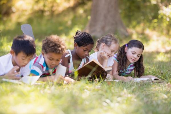 Group of friends reading book while lying on grassy field at campsite