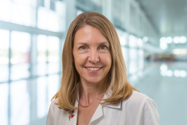 kori flower, woman with shoulder-length blond hair wearing lab coat stands in bright window-filled hallway