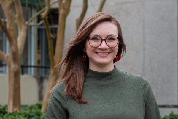 kylie garber; woman with shoulder-length brown hair and glasses wearing green sweater stands outside smiling at camera