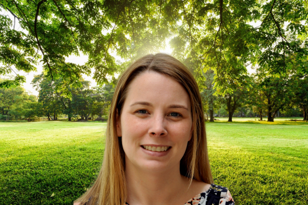 Laura Kuhn smiling at camera in front of grassy field and trees