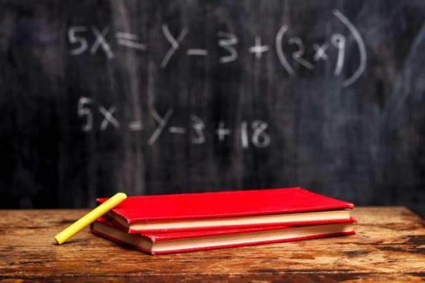 chalk board with math problems behind wooden desk with red notebooks on top