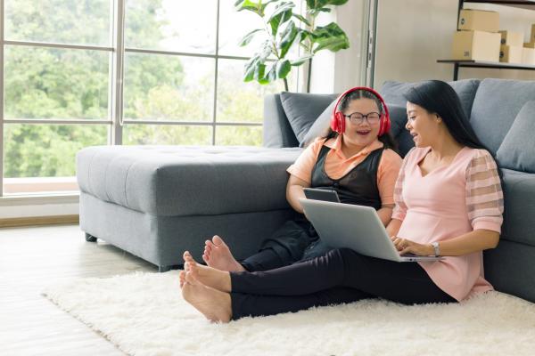 A mother and daughter working on laptop; woman with long dark hair sits beside pre-teen daughter leaning against couch with laptop in their laps | Credit: JuYochi