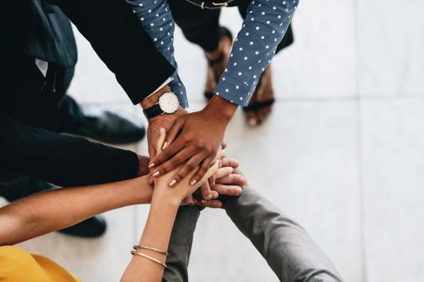 photo representing professional collaboration - several individual arms extended toward each other with hands stacked on top of each other