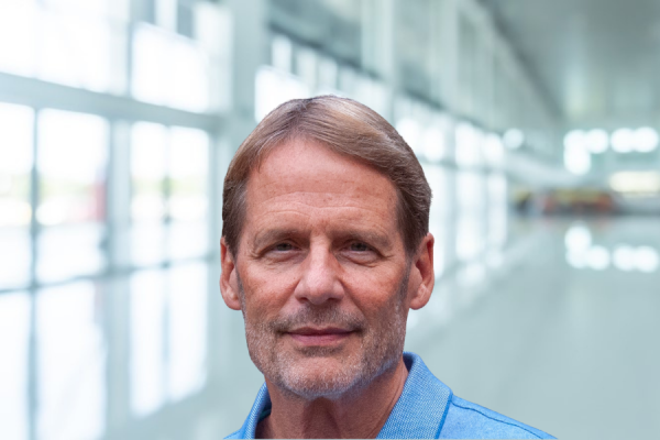 robin jenkins; man in light blue shirt stands in office hallway with bank of windows along the side