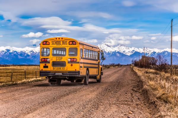 Yellow school bus on a country road, with snow-covered mountains in the background.